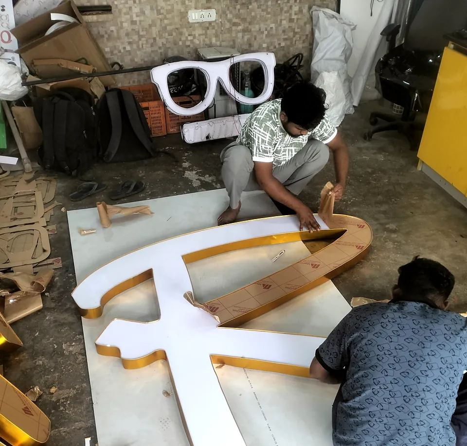 Two craftsmen assembling a large acrylic letter on the workshop floor