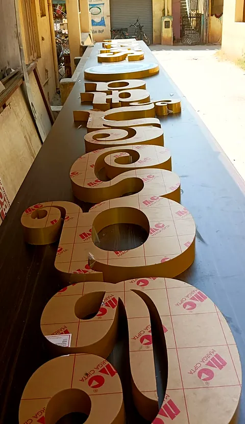 Gold-finish Kannada 3D letters laid out in the lane outside the workshop
