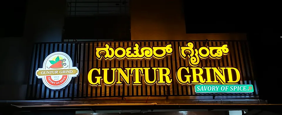 Guntur Grind restaurant board at night: gold backlit Kannada and English letters on black slats