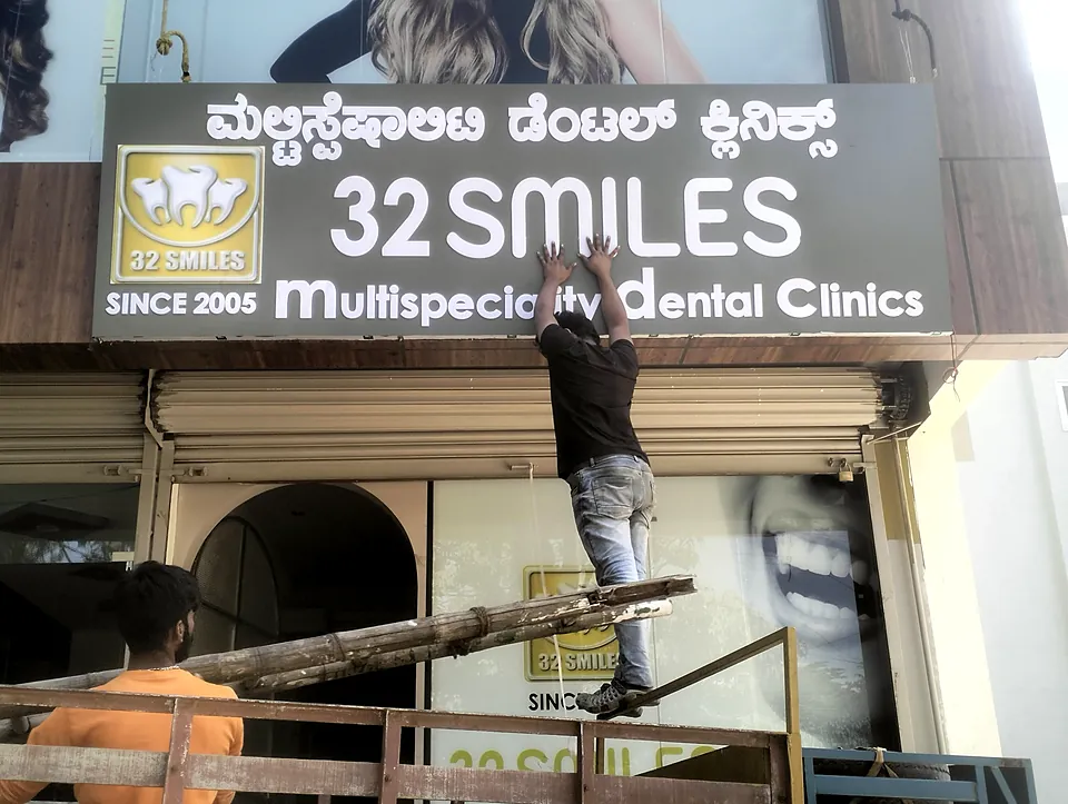 Moeen team fixing the 32 Smiles Multispeciality Dental Clinics board above a shop front