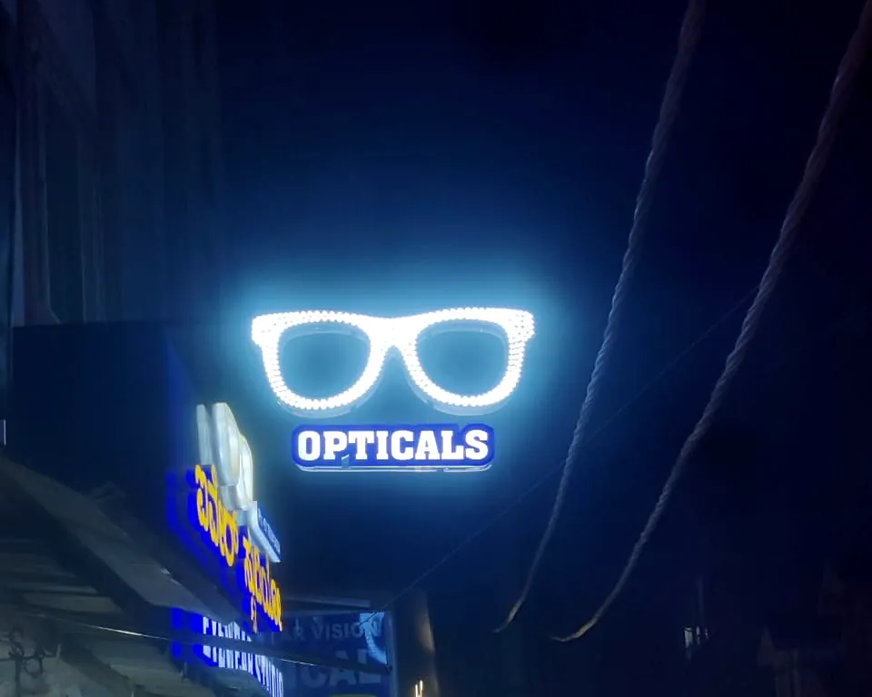 Glasses-shaped LED sign for an optical shop glowing over a busy street at night
