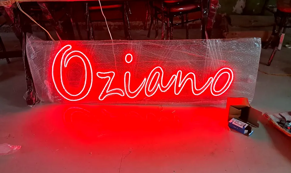Red neon Oziano script sign glowing in the workshop before delivery