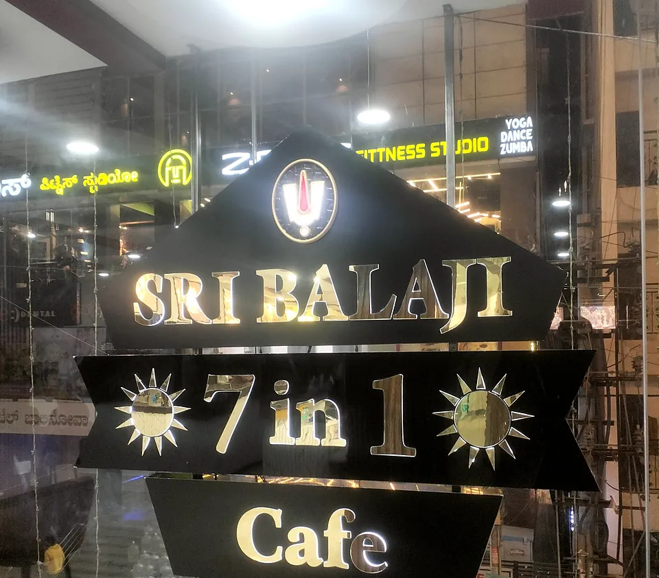 Sri Balaji 7 in 1 Cafe sign: gold acrylic letters on black cut panels behind glass