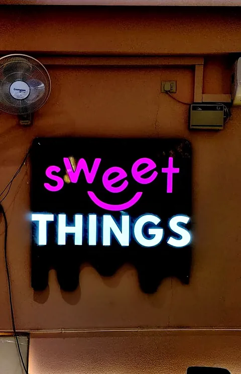 Sweet Things neon sign in pink and white on a dark drip-shaped backboard
